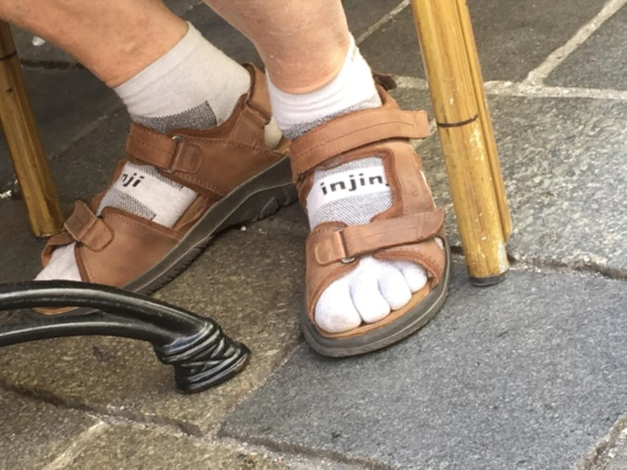 Feet in brown velcro sandals worn over white Injinji toe socks on a stone pavement