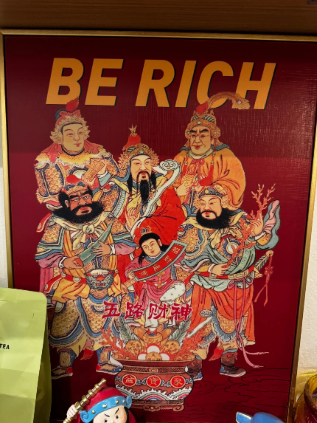 Framed red poster of five Chinese wealth gods with gold text reading "BE RICH" across the top